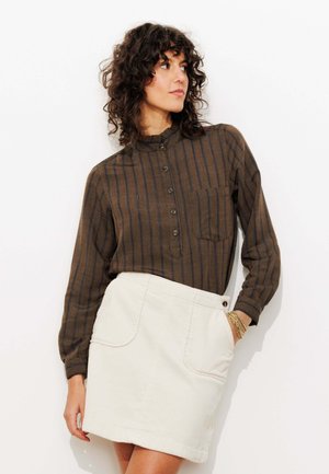 Chemise à rayures marron et bleues avec col mandarin, associée à une mini-jupe en velours côtelé crème dotée de deux poches avant.