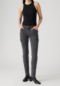 Top de tirantes negro canalé combinado con jeans cargo slim-fit gris oscuro que cuentan con bolsillos laterales y una textura suave, terminado con botas de tobillo negras.