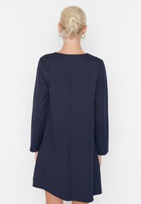 Robe longue à manches longues de couleur marine avec une silhouette droite, un tissu texturé et un col rond. Présente un subtil détail de couture à l'arrière.
