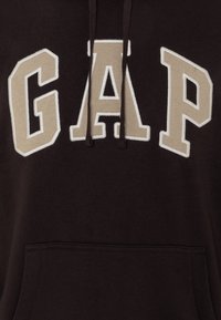 Felpa cappuccio marrone scuro con logo "GAP" ricamato color crema sul davanti, con cappuccio regolabile e tasca frontale. Tessuto morbido.