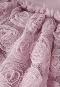 Lys rosa mesh-stoff med et mønster av 3D-roseapplikasjoner, med en rynket kant, som skaper et teksturert og lagdelt utseende.