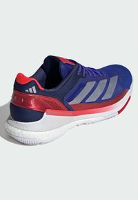 Blue athletic shoe with red accents, featuring a mesh upper, three silver stripes, and a textured sole. Durable material and modern design.