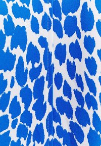 Niebiesko-biały materiał z wyrazistym, nieregularnym wzorem w panterkę o fakturowanej powierzchni. Szwy widoczne wzdłuż szwu.