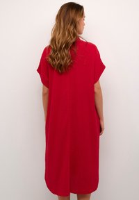 Abito rosso, dalla vestibilità ampia, realizzato in tessuto testurizzato. Presenta maniche corte e un orlo arrotondato, con un design semplice e pulito.
