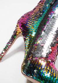 Hoge laarzen met hoge hak, bedekt met meerkleurige pailletten; voorzien van een rits aan de zijkant en een puntige neus. Gladde textuur met glanzende, reflecterende oppervlakken.