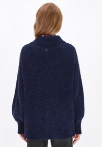 Navyblauwe, zachte gebreide trui met een hoge kraag en een losse pasvorm. Kenmerkt breed mouwen en een langere achterzoom met een klein logo-label.