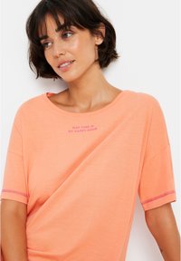 Peach-colored cotton T-shirt with short sleeves, featuring a relaxed fit and pink text that reads "NAP TIME IS MY HAPPY HOUR" on the chest.