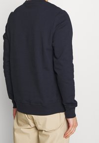Sudadera de color azul marino con cuello y puños de punto, hecha de una tela suave. La parte trasera presenta un diseño limpio sin logotipos o patrones visibles.
