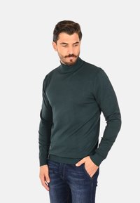 Maglione dolcevita verde scuro in tessuto a maglia liscia, con design aderente e polsini e orlo a coste, abbinato a jeans blu.