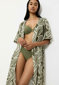 Długi, luźny kimono w zielono-białym abstrakcyjnym wzorze, z krótkimi rękawami i otwartym przodem. Modelka ma na sobie dopasowany kostium kąpielowy.