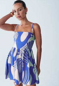 Sininen ja valkoinen kuvioitu mekko, jossa on istuva yläosa ja leveä helma; sisältää ohuet olkaimet ja sileän pinnan.