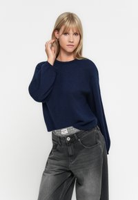 Marineblauwe gebreide trui met een ronde halslijn, een ontspannen pasvorm en lange mouwen, gecombineerd met hooggepongeerde vervaagde zwarte jeans.