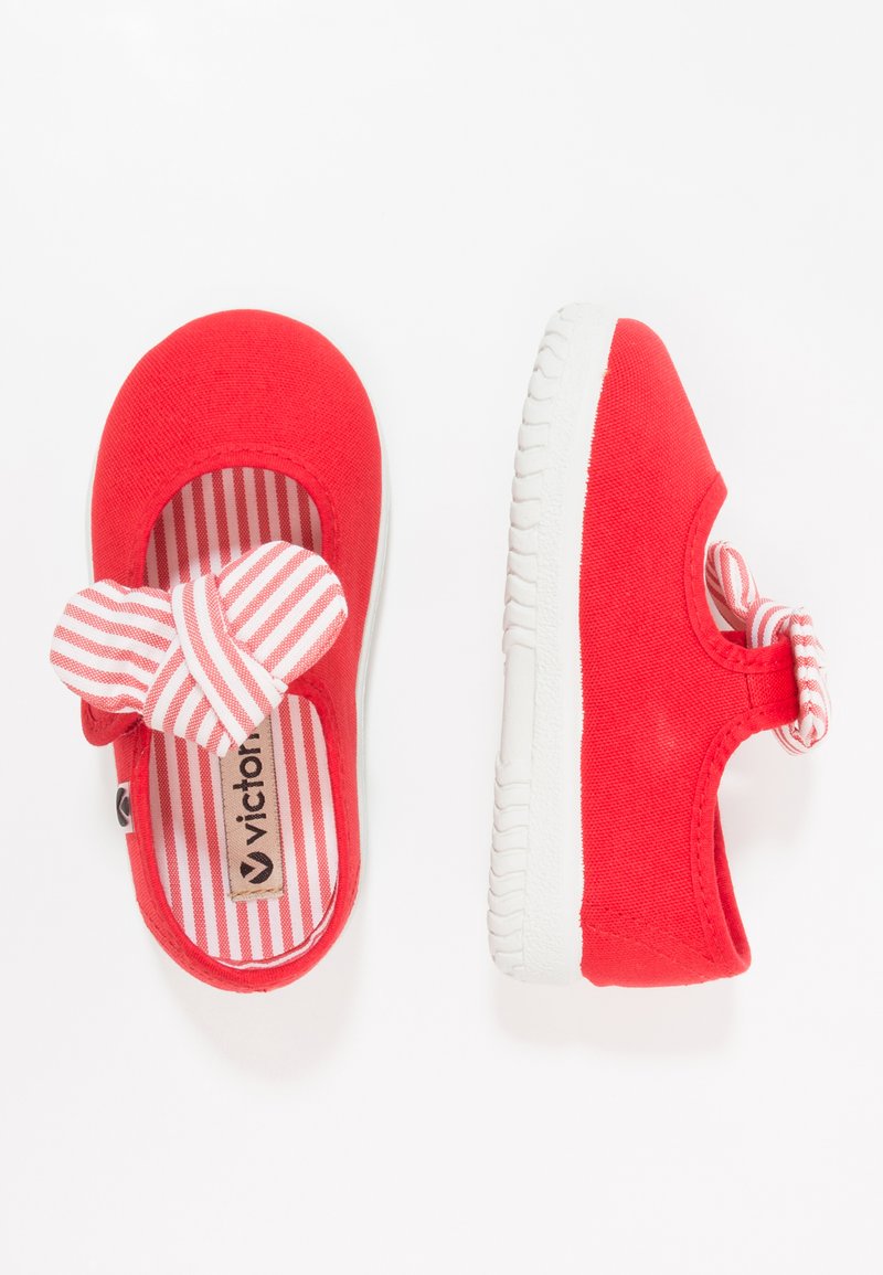 Par de zapatos rojos para niños pequeños con suelas blancas, que cuentan con un interior a rayas y un lazo de tela a rayas en la correa.