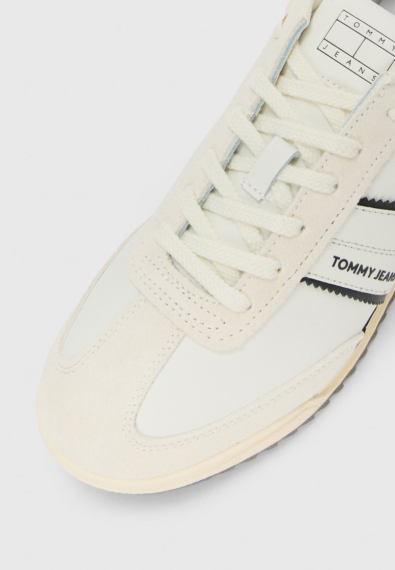 Baskets blanches et crème avec des panneaux en daim texturé, lacets blancs et marquage "Tommy Jeans" sur le côté et la languette.