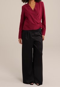 Blusa avvolgente color bordeaux con maniche lunghe e dettaglio nodo laterale, abbinata a pantaloni neri a righe larghe e sandali neri con punta aperta.