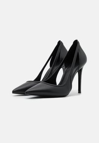 Escarpins noirs à talons hauts avec bouts pointus, côtés découpés, en cuir, dotés d'un design élégant avec un talon stiletto.