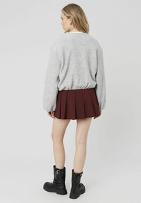 Un pull gris texturé avec un ourlet resserré, associé à une jupe plissée bordeaux. Des bottes noires jusqu'au genou avec des accents à boucles.