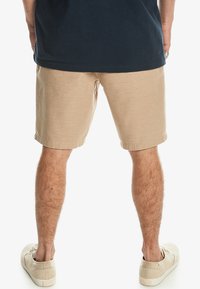 Beige shorts med en texturerad tyg, rak passform, rullad fåll och sidofickor. Kombinerat med ljusa sneakers.