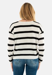 Maglione a righe bianco e nero, con vestibilità ampia, spalle ripiegate e texture a coste, abbinato a jeans blu aderenti.