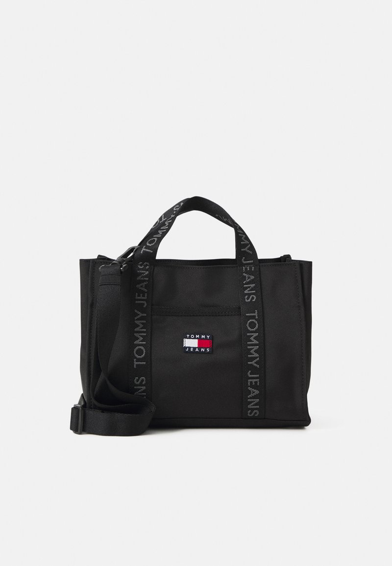 Musta kantokassi, jossa on tekstuuripintainen kangas, kaksi lyhyttä kantohihnaa ja irrotettava olkahihna. Koristeltu "TOMMY JEANS" -brändillä ja logo-patchilla.