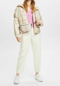 Beige-toppatakki, vaaleanpunainen neuletakki, valkoiset housut ja valkoiset tennarit. Vaaleanvärinen olkalaukku on kiinnitetty vyötärölle.