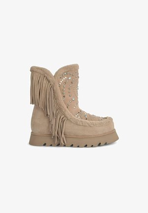Bottine en suède beige avec des détails en franges, ornée de studs en argent, dotée d'une semelle texturée pour une meilleure adhérence et d'un doublage en fourrure douce.