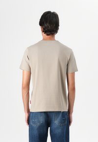 Beige short-sleeve t-shirt with a round neckline. Smooth cotton fabric with a slight stretch, featuring a small red tag at the side seam.