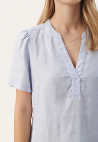 Svijetloplava lanena bluza s V-izrezom, kratkim rukavima s nabranim detaljima na ramenima i ravnim krojem. Teksturirana tkanina.