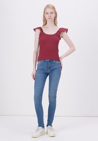 Burgundy knitted top with lace trim at shoulder, fitted design, paired with light blue skinny jeans and white sneakers.