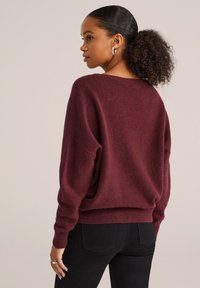 Bordeaux oversized trui met verlaagde schoudernaden, geribde manchetten en zoom. Zachte, gestructureerde stof gecombineerd met slim fit zwarte jeans.