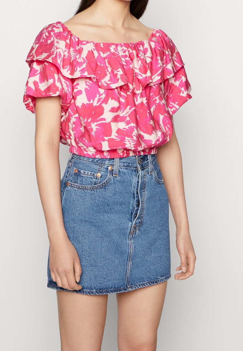 Blouse rose à motifs floraux, épaules dénudées, avec des manches volantées, associée à une jupe en denim ajustée avec fermeture par boutons et ourlet effiloché.