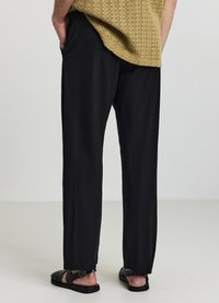 Schwarze, locker sitzende Hose aus leichtem Material, mit geradem Schnitt und Seitentaschen, kombiniert mit schwarzen Sandalen.