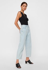 Μαύρο τοπ με δαντέλα, ανοιχτό μπλε ψηλόμεσα τζιν, μαύρα σανδάλια με ανοιχτά δάχτυλα και τακούνι block. Καθημερινό σύνολο παρουσιάζεται σε μοντέλο.