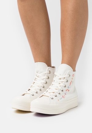 Sneaker alte in tela bianca con motivi floreali ricamati, punta rotonda e suola in gomma testurizzata. Presenta occhielli in metallo e lacci.