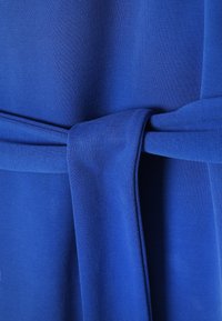 Gros plan sur un tissu bleu royal texturé noué simplement, montrant le tissage et les plis du tissu.
