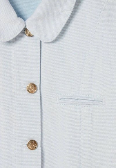 Chemise en denim bleu clair avec un col arrondi, des boutons dorés et un petit détail de poche brodée sur la poitrine.