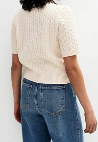 Kermanvärinen kaapeli-neulottu lyhythihainen neulepaita, jossa on ribbahemmo, yhdistettynä korkeavyötäröisiin sinisiin farkkuihin, joissa on läppätaskut.