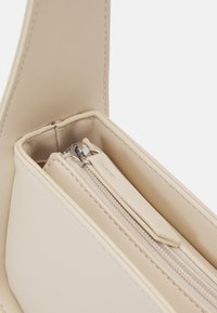 Gros plan de l’intérieur d’un sac en cuir beige montrant des bords cousus et une pochette zippée avec une languette en cuir.