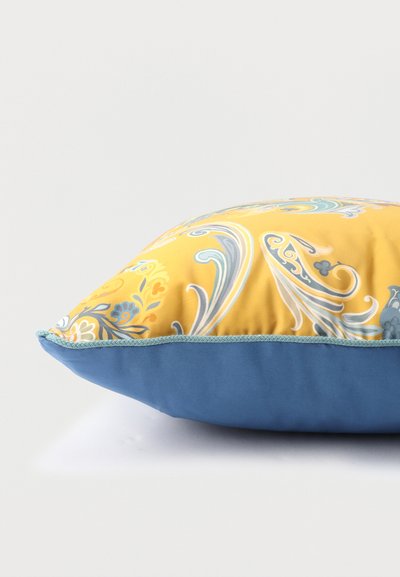 Coussin avec dessus jaune présentant des motifs floraux paisley bleus et gris, dessous bleu, et bordure tressée bleu clair le long des bords.