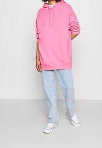 Rosa överdimensionerad hoodie med dragsko i huooden, kombinerad med ljusblå raka jeans och vita sneakers. Mjuk tyg, avslappnad passform.