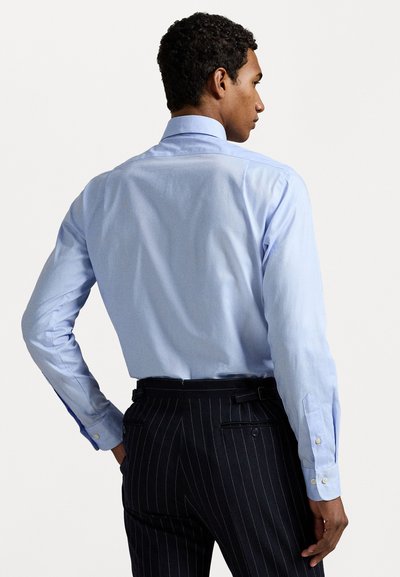 Camisa de manga comprida azul clara com uma textura suave e yoke nas costas; formato ajustado combinado com calças listradas escuras com passadores para cinto.