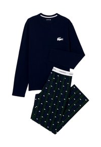 Námořnická modrá košile s dlouhým rukávem a bílým logem krokodýla, spárovaná s kalhotami s tmavě zeleným a modrým kostkovaným vzorem, které mají bílé tisky krokodýla a značku Lacoste.