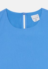 Modrá bavlnená blúzka s okrúhlym výstrihom, zadným zapínaním na kľúčovú dierku a štítkom označujúcim veľkosť 9/10. Hladká textúra s jednotnou farbou.