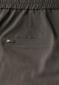 Tissu léger gris foncé avec une texture lisse. Comprend une taille élastique et une poche arrière unique avec une petite étiquette logo en métal.
