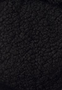 Textil negro y esponjoso con una superficie densa y texturada. Presenta una sensación suave y aterciopelada, con un color profundo y consistente en todo su superficie.