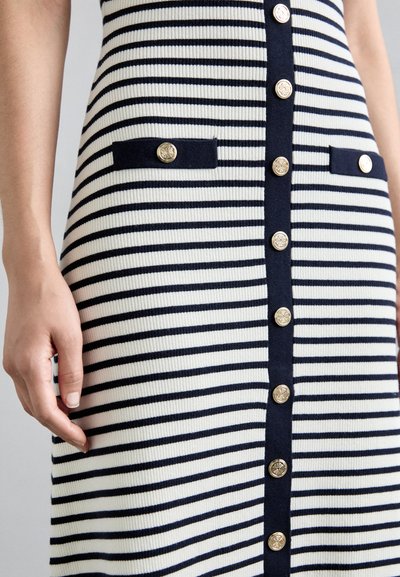 Strickkleid mit vertikalen blau-weißen Streifen, sechs goldenen Knöpfen an der Vorderseite und zwei blauen Taschen mit goldenen Akzenten.