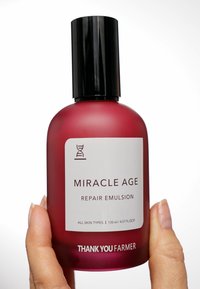 Glasflaska med en gradientröd finish, svart skruvkork, vit etikett som visar "MIRACLE AGE REPAIR EMULSION," 130 ml kapacitet.