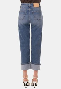 Jeans in denim blu con vita alta, gamba dritta, orli ripiegati e due tasche posteriori. Presentano un'etichetta in pelle marrone sulla cintura.