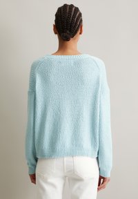 Helles blaues gestricktes Sweatshirt mit strukturiertem Muster, überschnittenen Schultern und geripptem Saum, kombiniert mit weißen hochgeschnittenen Jeans.