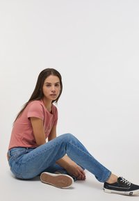 Camisa de manga corta rosa con cuello redondo, combinada con pantalones vaqueros rectos de color azul claro y zapatillas negras con acentos blancos.